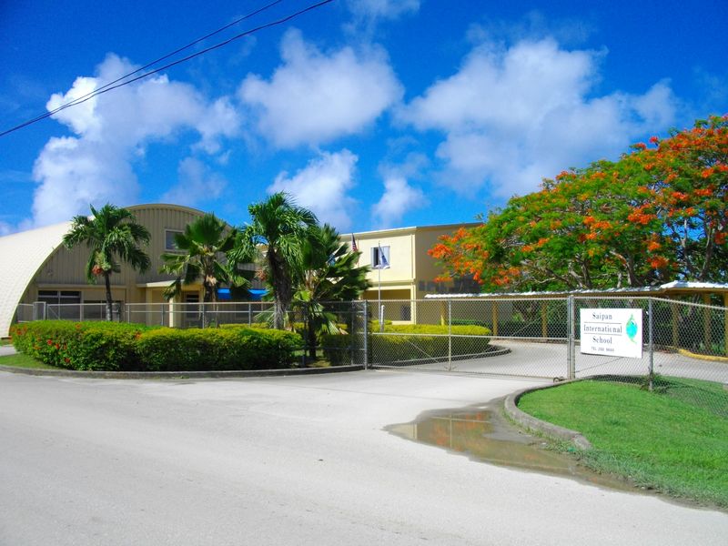The entrance to Saipan International School, with palm trees and a flame tree in red bloom